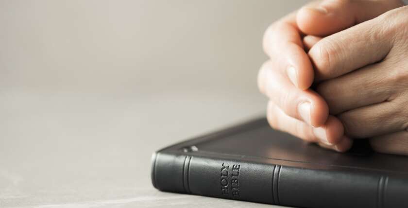 Hands closed in prayer on Holy Bible. Christian banner with copy space. Prayer and gospel spreading